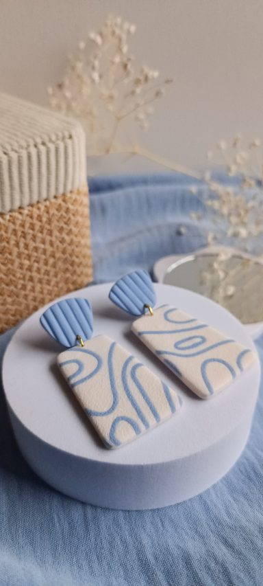 Boucles d'oreilles en céramique avec motifs ondulés bleus et jaunes sur fond clair.