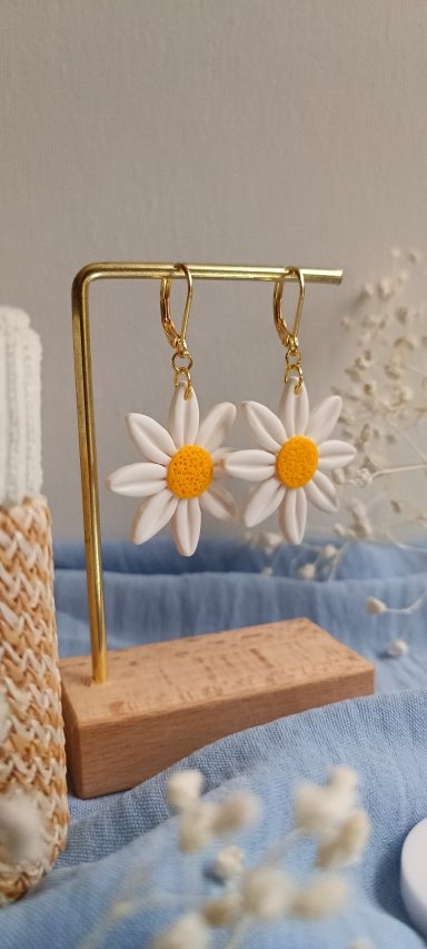 Boucles d'oreilles en forme de marguerites blanches avec un centre jaune.
