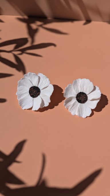 Paires de fleurs blanches avec un centre noir sur fond orange. Ombres de feuilles visibles.
